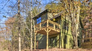 Une cabane dotée d’une terrasse en bois et d’une fenêtre donnant sur une forêt.