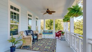 A covered porch with wicker furniture, a ceiling fan, and a view of the surrounding greenery. - Harbor Oaks Haven: Walk to Front Beach & Downtown! (Ocean Springs)