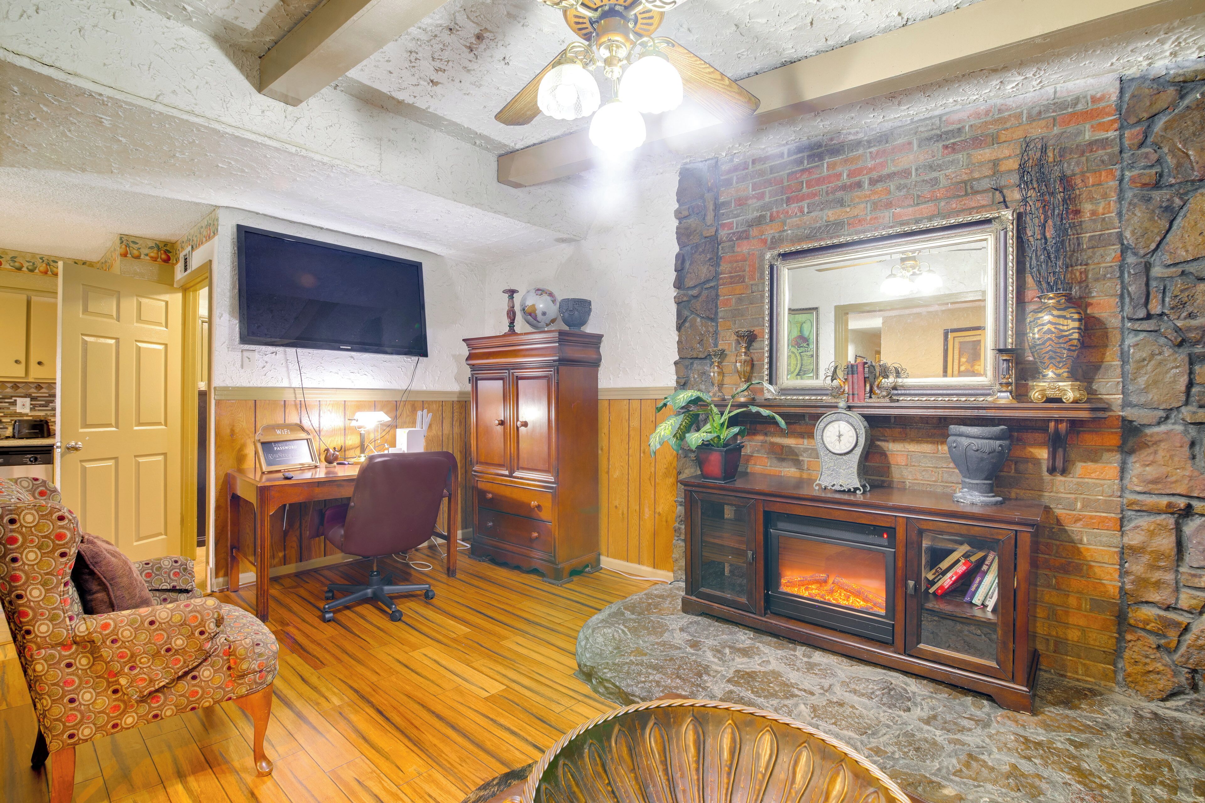 A cozy living room with a fireplace, wooden flooring, a stone accent wall, a television, and a desk with a computer.