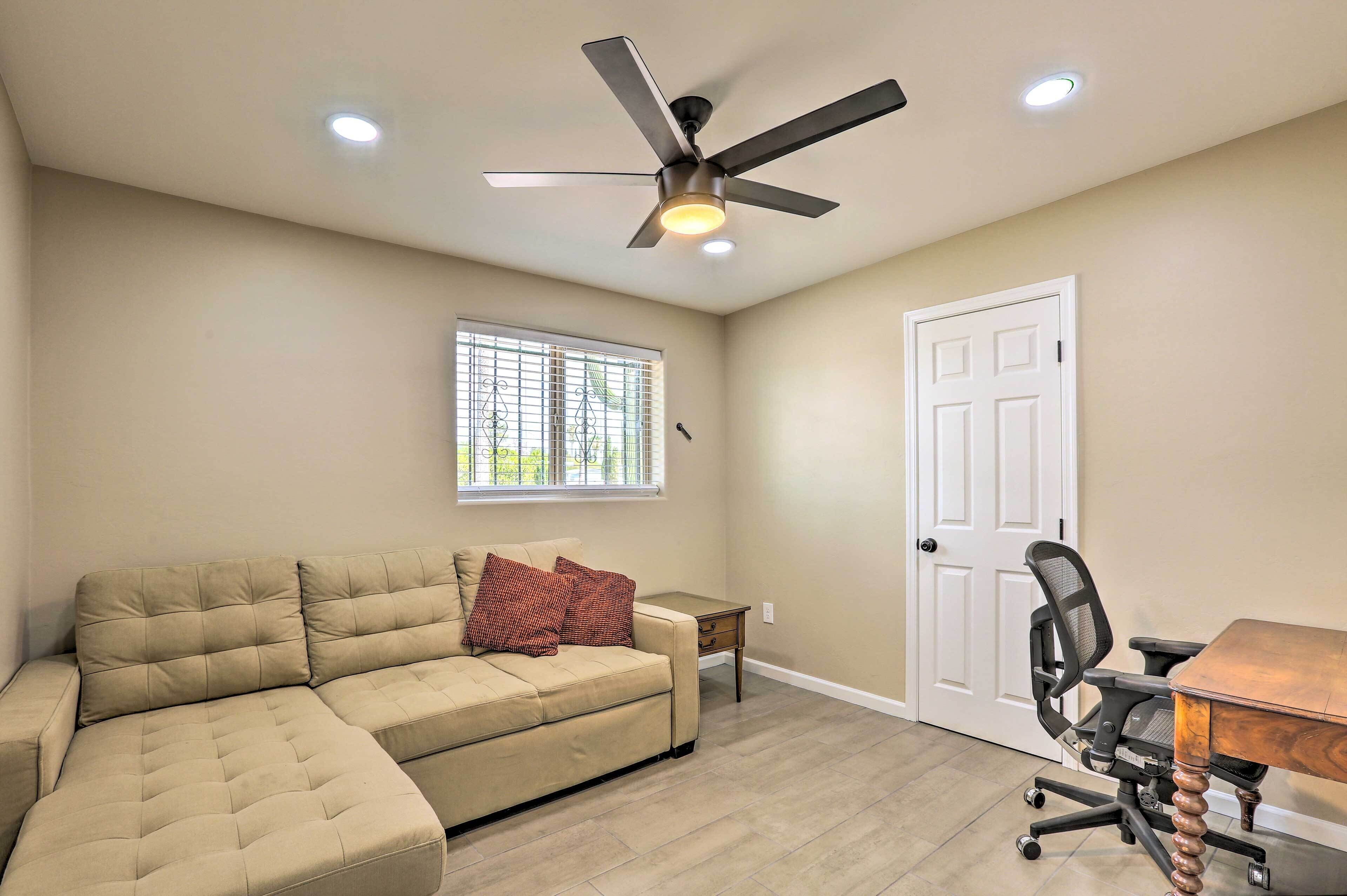 A room with a sectional sofa, a ceiling fan, a small table, a chair, and a door.