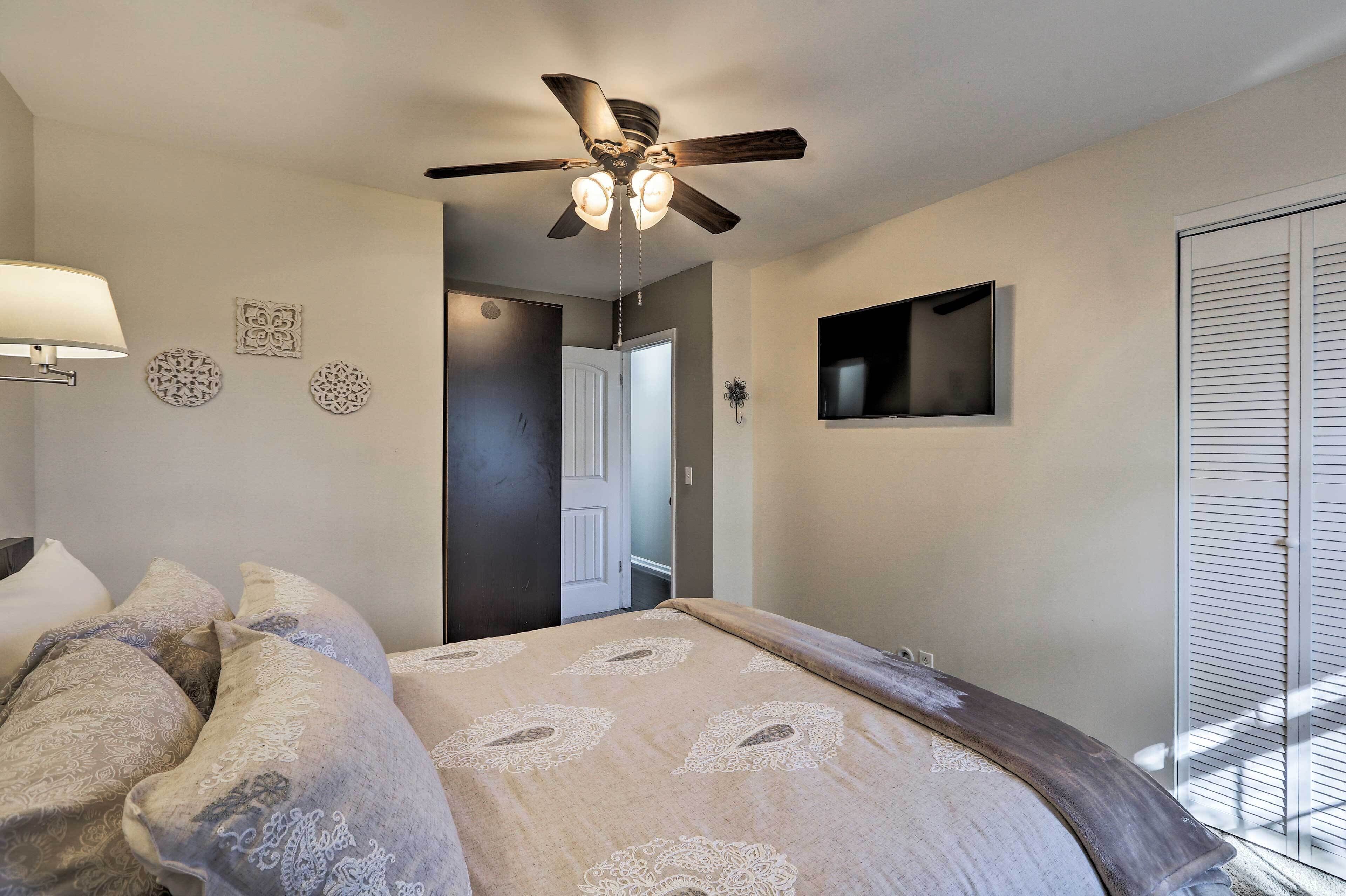 A bedroom with a bed, a ceiling fan, a TV, and a door leading to another room.