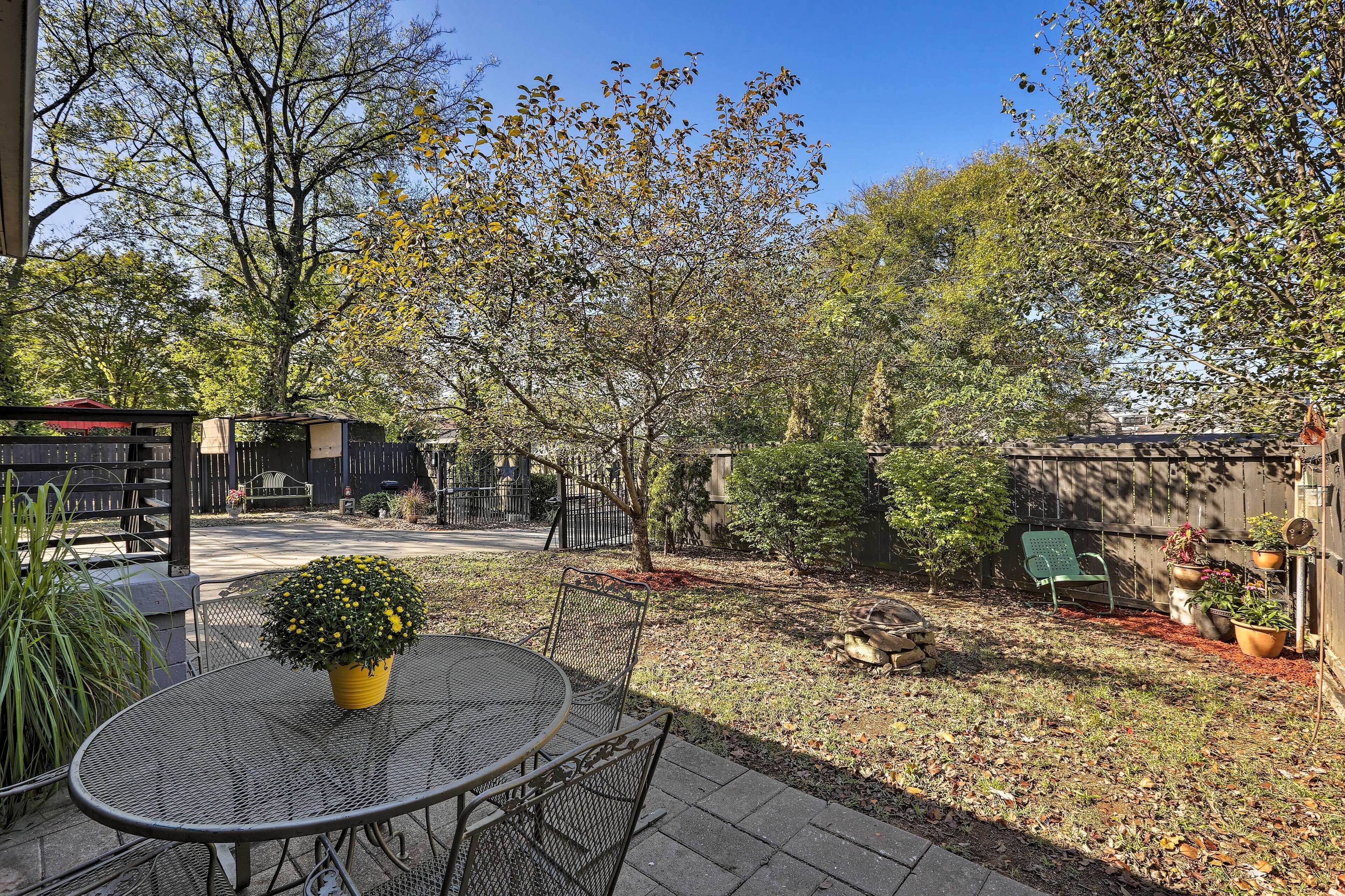 A patio area with a round metal table and chairs, surrounded by potted plants and a small tree.