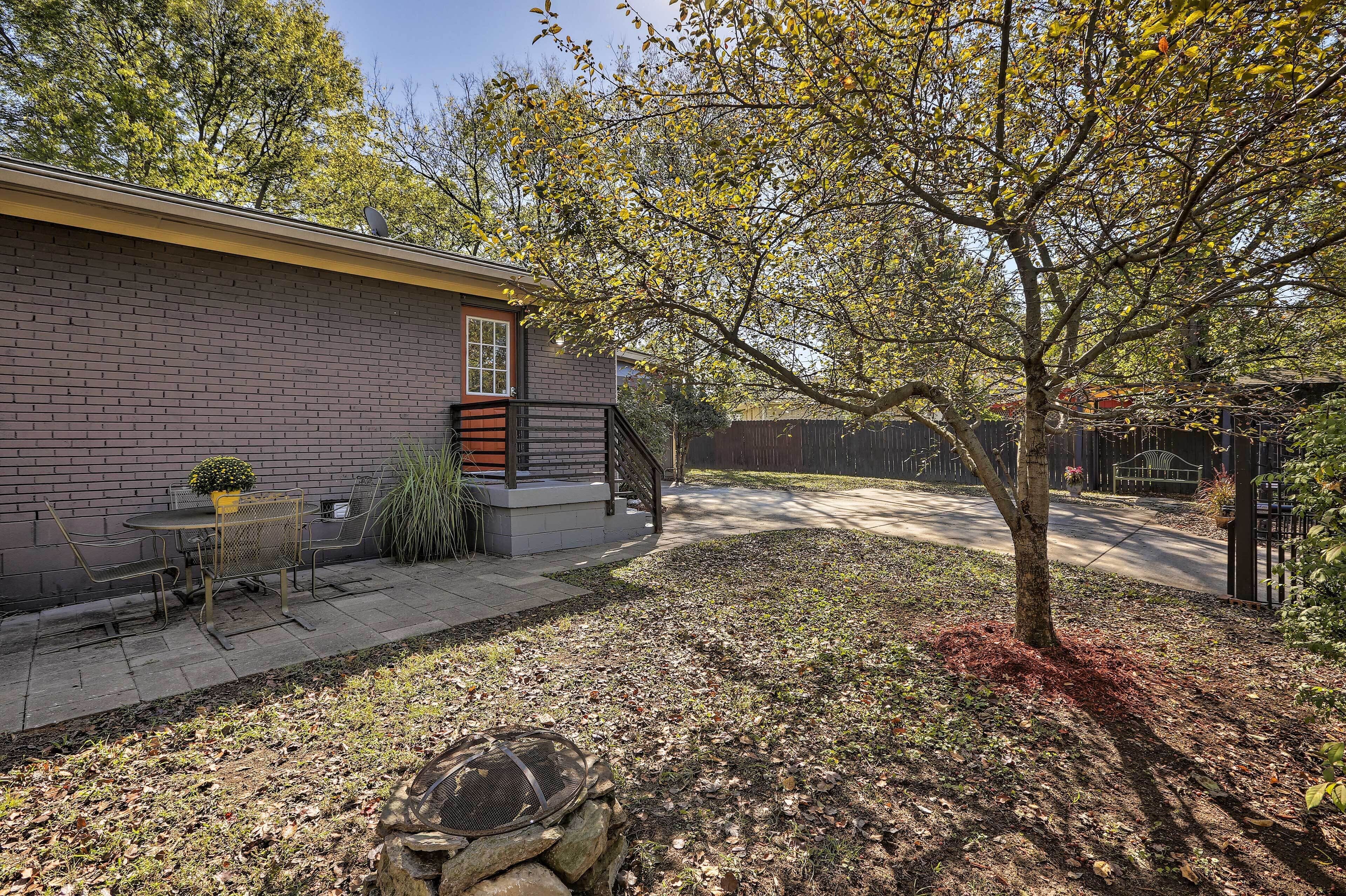 A brick house with a patio, a small table and chairs, a tree, and a fence.