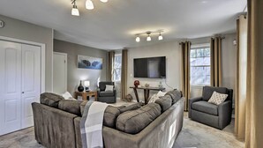 Un salon moderne comprenant un canapé d’angle, un fauteuil, un téléviseur à écran plat et une petite table d’appoint.