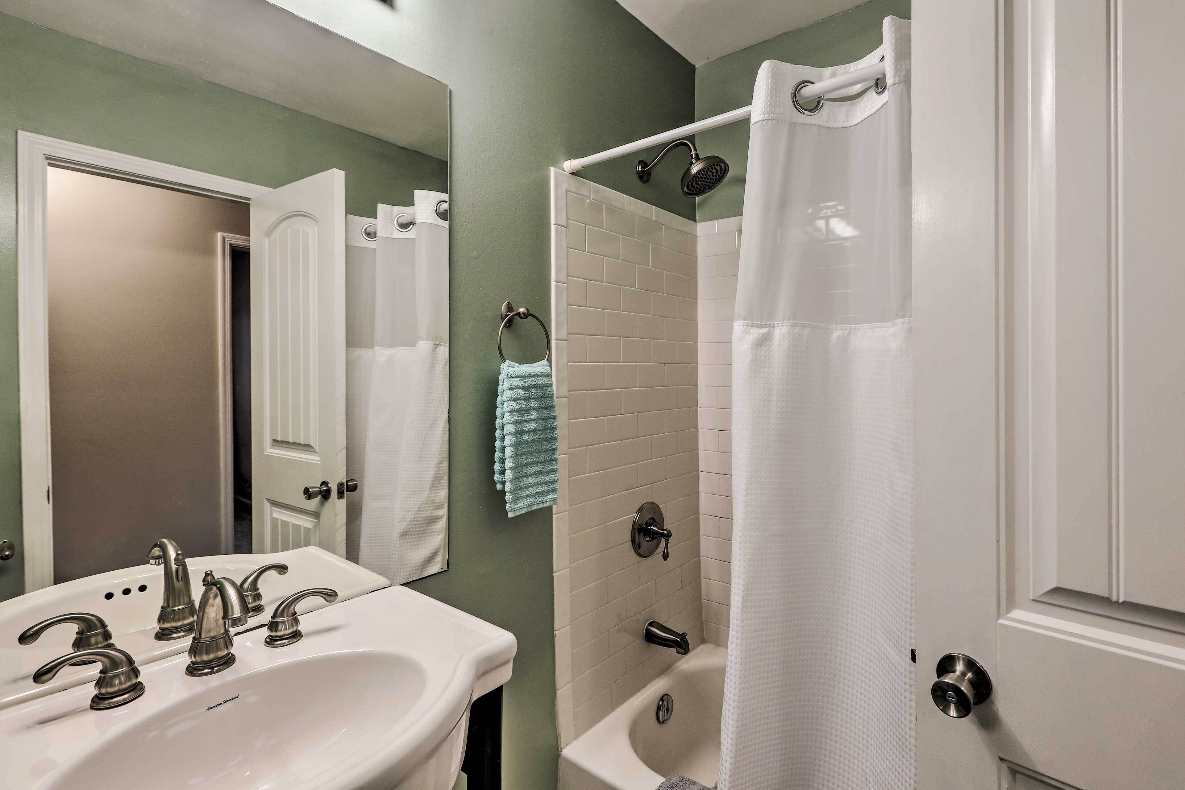 A bathroom with a white sink, two faucets, a mirror, a white bathtub, and a shower curtain.