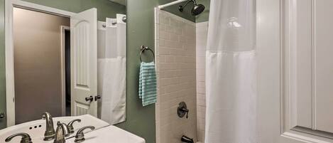 A bathroom with a white sink, two faucets, a mirror, a white bathtub, and a shower curtain.