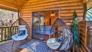 A log cabin with two wicker chairs on a wooden deck, a glass door leading inside, and a Christmas tree. - Cherry Lake Lodge w/ Hot Tub, Fire Pit & Game Room (Blue Ridge)