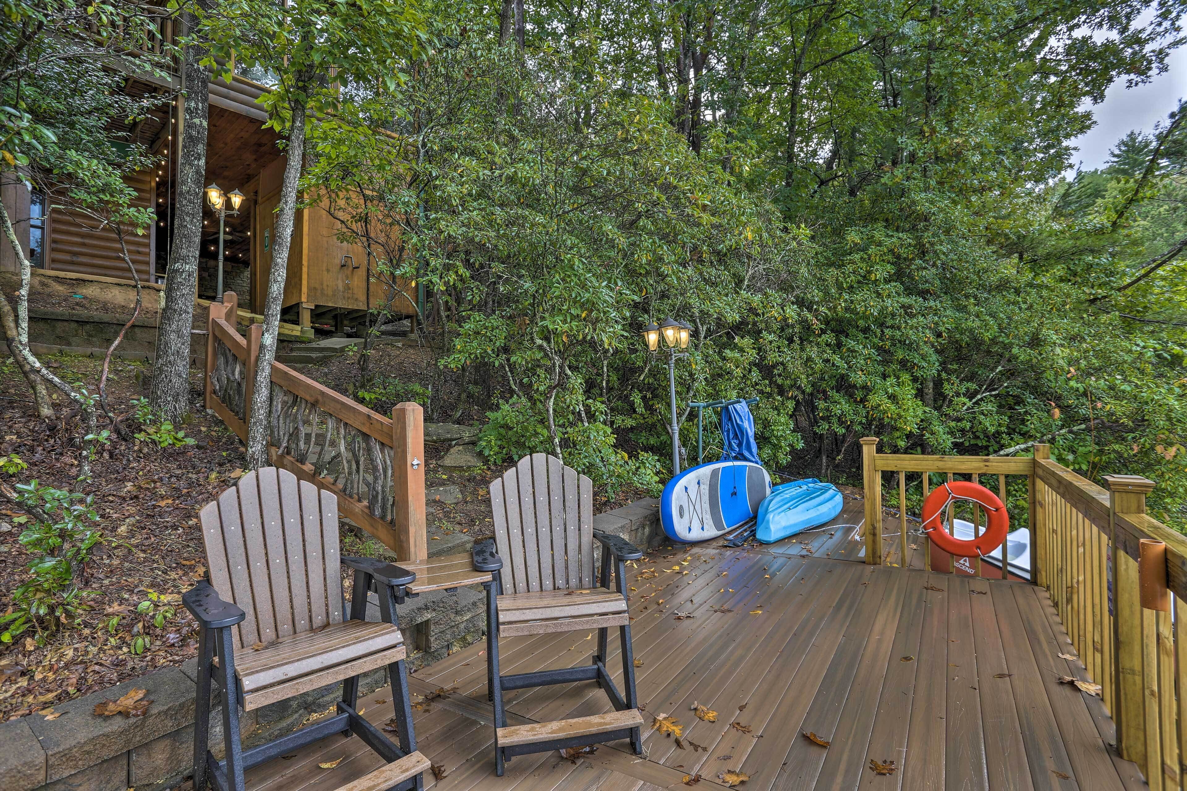 Una terraza de madera con dos sillas Adirondack, un flotador salvavidas y un kayak azul.