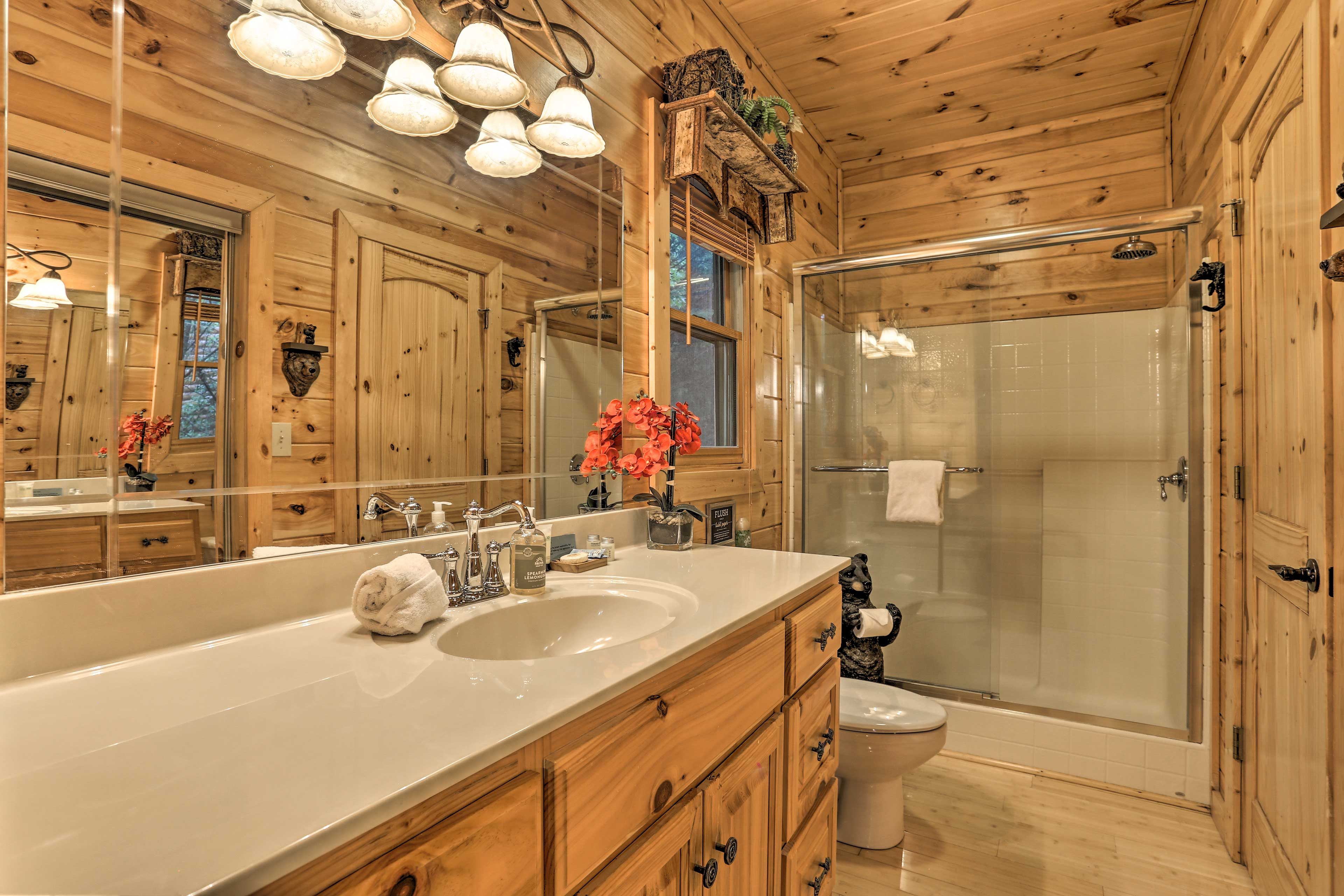 Une salle de bain rustique, avec des murs en bois, comprenant un grand miroir, un lavabo, des toilettes et une douche à parois de verre.