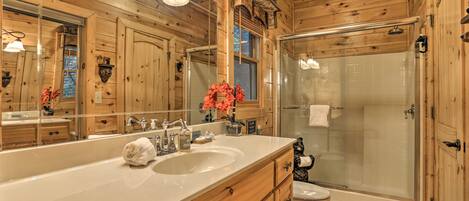 Une salle de bain rustique, avec des murs en bois, comprenant un grand miroir, un lavabo, des toilettes et une douche à parois de verre.
