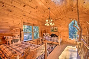 A cabin with two beds, a chandelier, and a large window offering a view of the forest. - Cherry Lake Lodge w/ Hot Tub, Fire Pit & Game Room (Blue Ridge)