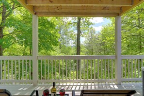 A wooden deck with a white railing, overlooking a forested area.