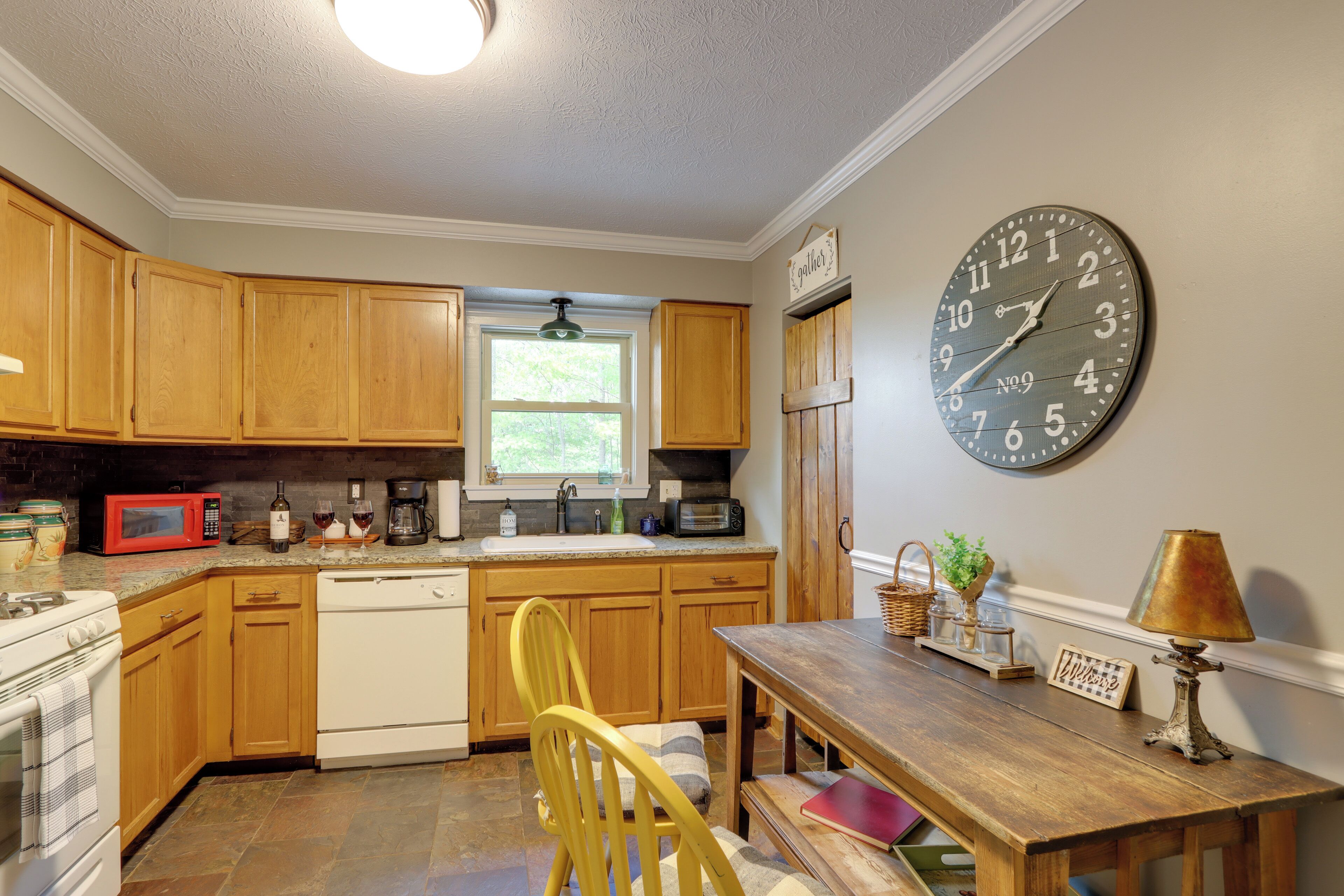 Une cuisine avec des meubles de rangement en bois, une cuisinière, un four à micro-ondes et une horloge au mur.