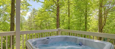 A hot tub on a wooden deck with a view of a forest.
