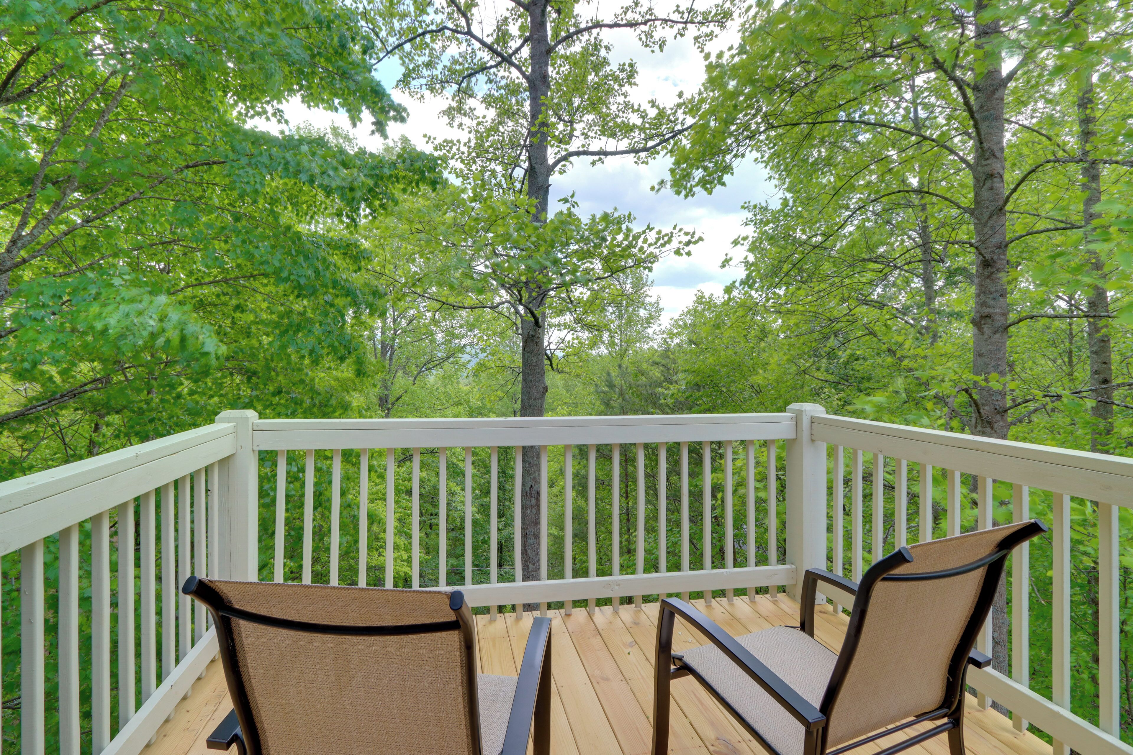 A wooden deck with white railings and two chairs facing a forested area.