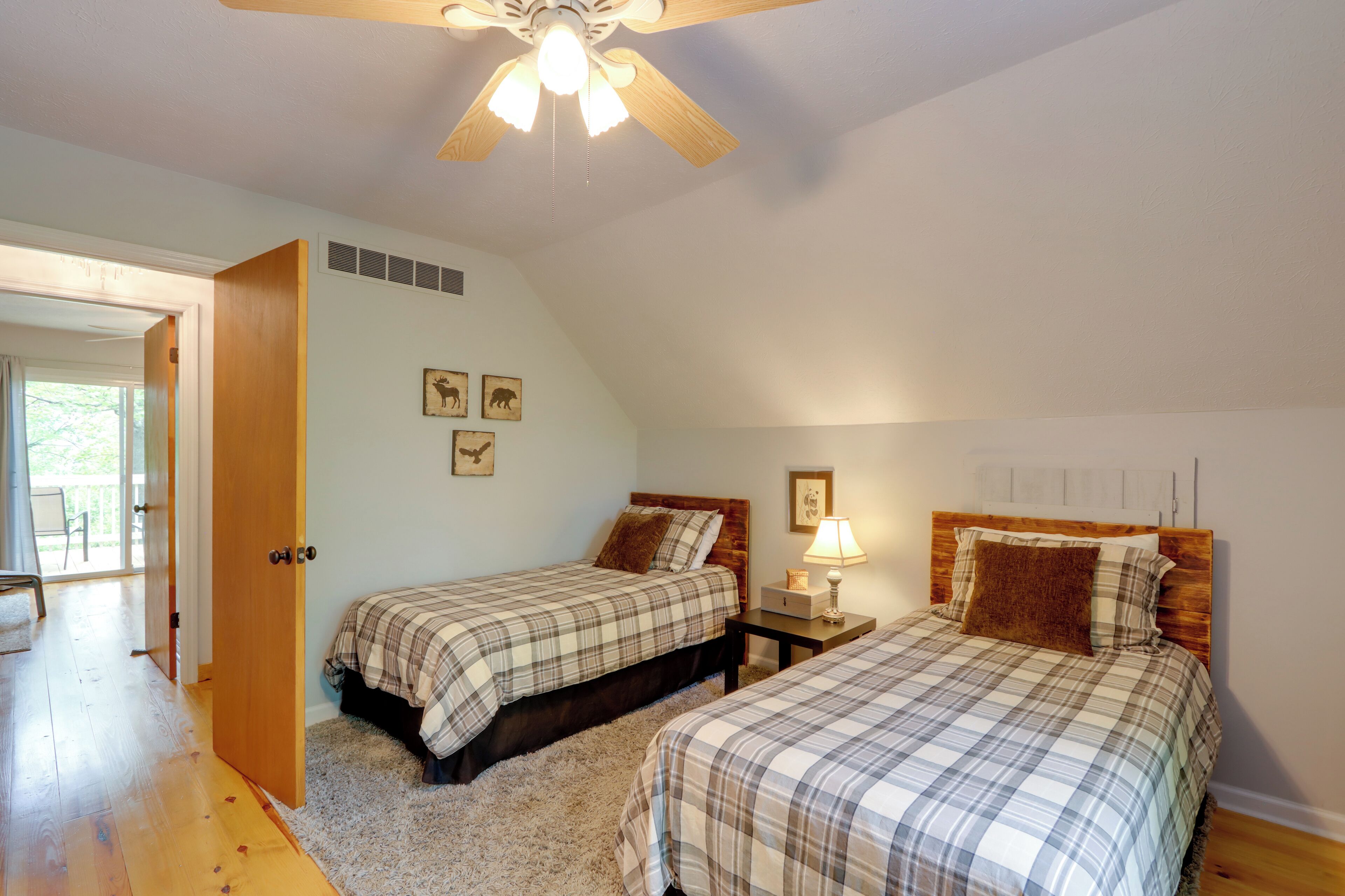 A bedroom with two beds, a ceiling fan, a nightstand with a lamp, and a door leading to a balcony.