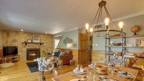 A cozy living room with a fireplace, a dining area set for a meal, and a television in the corner. - Blue Ridge Getaway w/ Hot Tub & Seasonal View! (Blue Ridge)