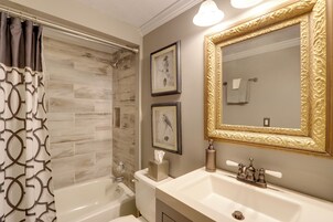 Un baño con una bañera, un lavamanos y un espejo grande con un marco decorativo. Hay dos cuadros en la pared.