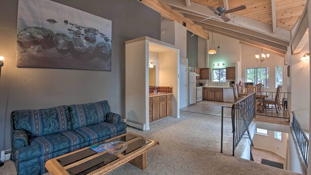 A spacious living area with a sofa, coffee table, and artwork on the wall. A kitchen and dining area are visible in the background. - Stateline Ski House: Walk to Boulder Lift! (Stateline)