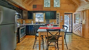 Une cuisine rustique, située dans une cabane en bois, équipée d’un réfrigérateur, d’un four et d’une table avec des chaises.