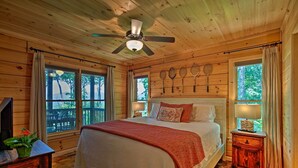 Une chambre dans une cabane en bois, avec un lit, un ventilateur de plafond et des fenêtres avec des rideaux.