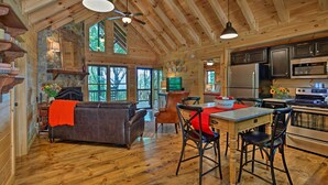 L’intérieur chaleureux d’un chalet avec un plafond en bois, un coin repas comprenant une table et des chaises, un canapé et une cuisine équipée.