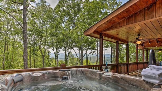 Un bain à remous doté d’une cascade, entouré d’une terrasse en bois et offrant une vue sur une zone boisée.