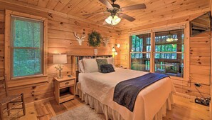 A wooden cabin bedroom with a bed, nightstands, a ceiling fan, and a window with blinds.
