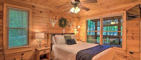 A wooden cabin bedroom with a bed, nightstands, a ceiling fan, and a window with blinds.