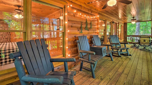 A wooden cabin interior with a porch, Adirondack chairs, and string lights.