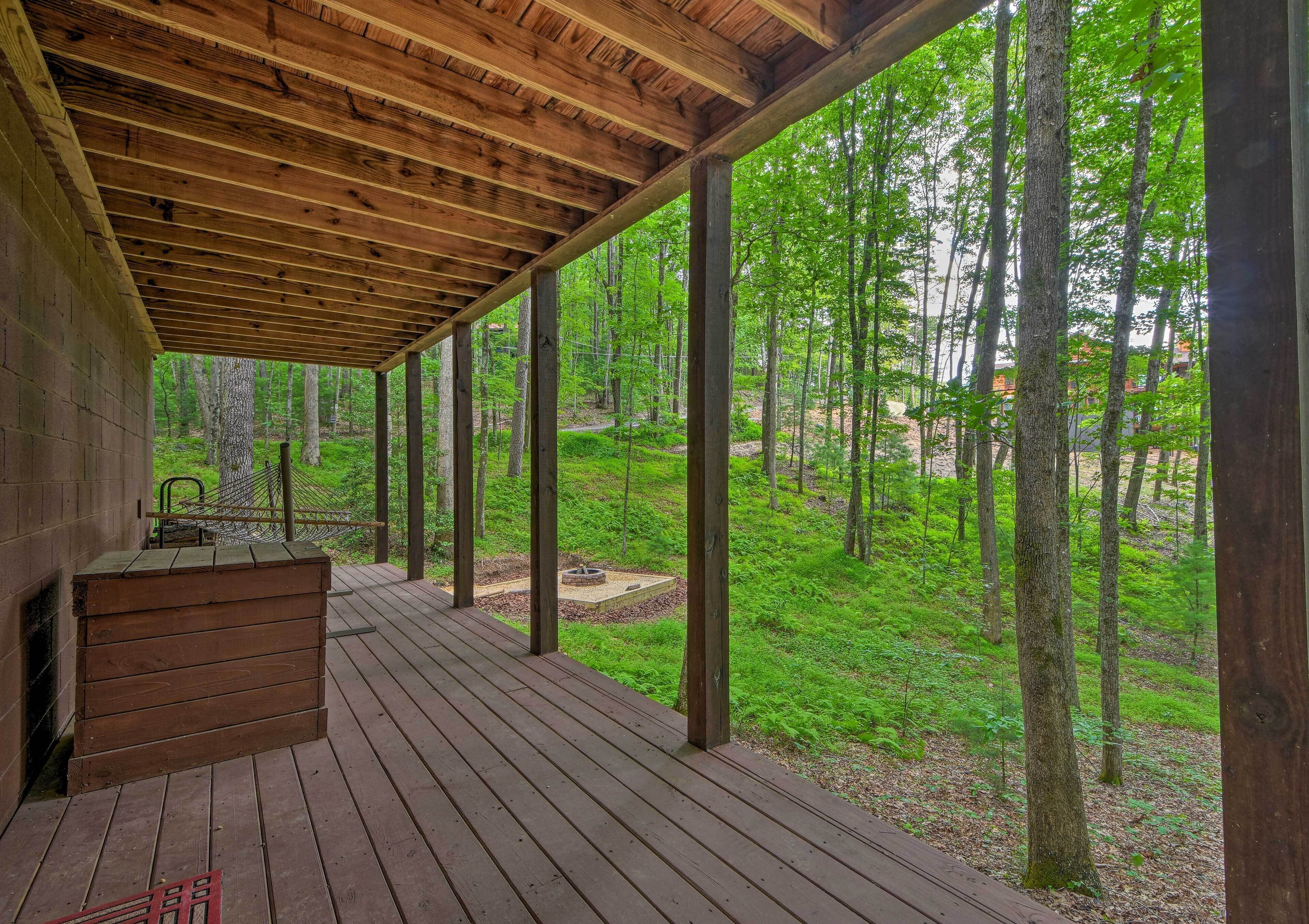 A wooden deck with a built-in grill area, surrounded by a forested landscape.