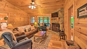 A cozy cabin interior with a wooden ceiling, a fireplace, a television, and a comfortable seating area.