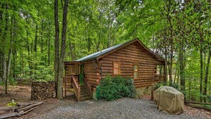 A log cabin with a covered porch, a stone wall, and a gravel driveway.