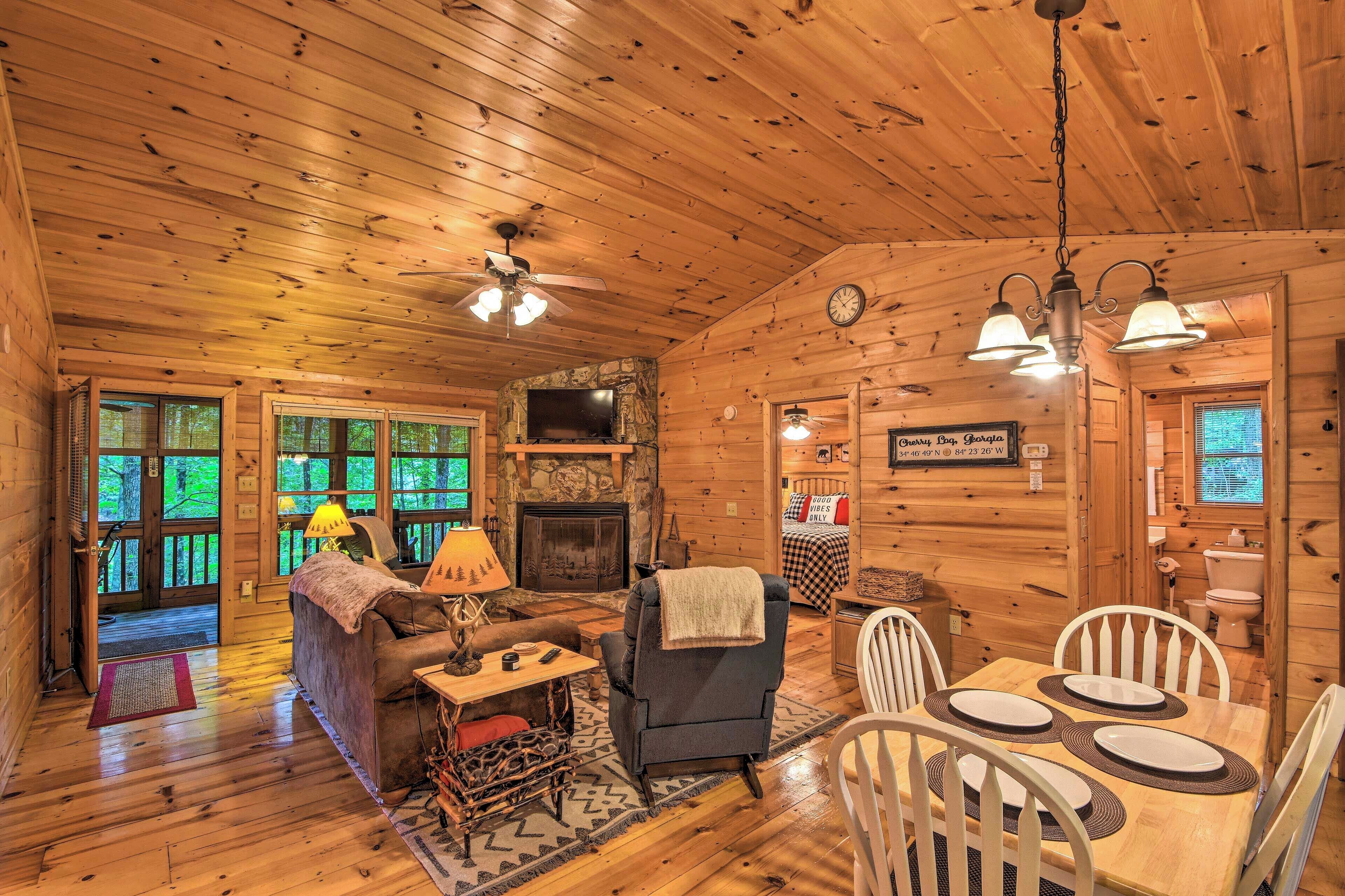 Interior acogedor de una cabaña con chimenea, paredes de madera, una zona de comedor y una sala de estar con sofá y lámpara.