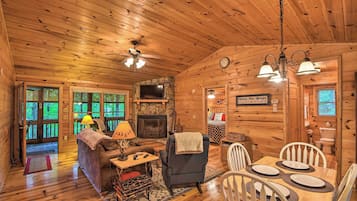 Interior acogedor de una cabaña con chimenea, paredes de madera, una zona de comedor y una sala de estar con sofá y lámpara.