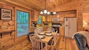 A cabin-style kitchen with wooden walls and ceiling, a dining table with chairs, a refrigerator, and a microwave.