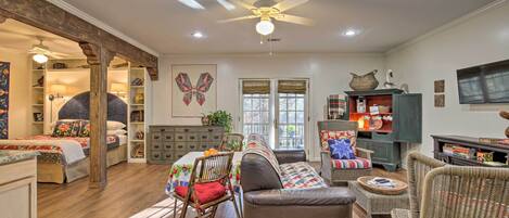 A spacious living room with a brown leather sofa, wicker chairs, a dining table with chairs, and a ceiling fan.