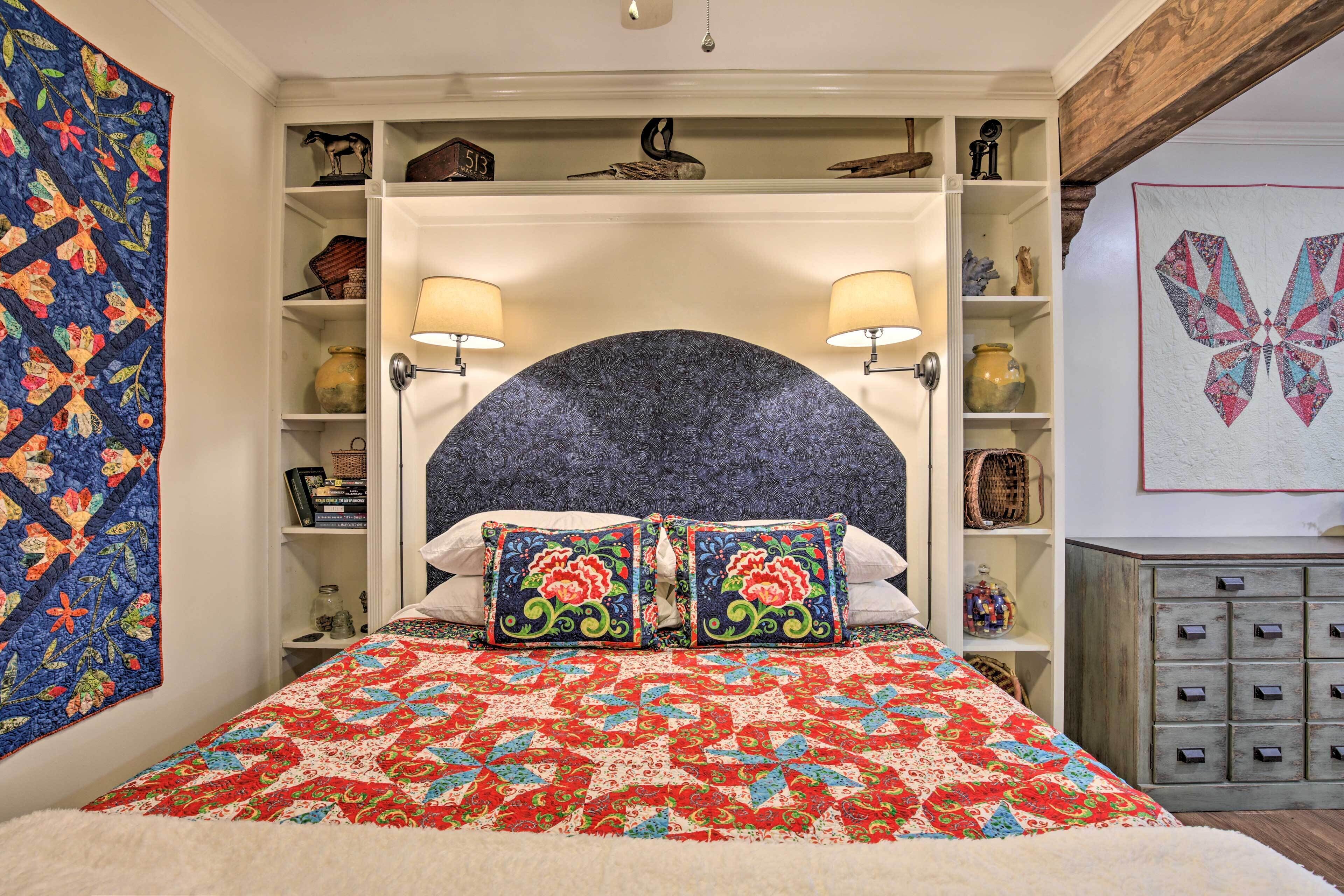 A bedroom with a large bed, two wall-mounted lamps, a decorative headboard, and shelves with various items.