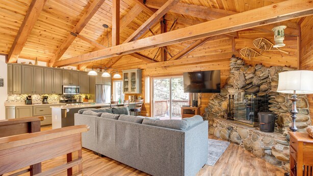 A spacious living area with a stone fireplace, wooden beams, and a large gray sectional sofa. - 4 Mi to Beach: Lake Tahoe Mountain Retreat! (Stateline)