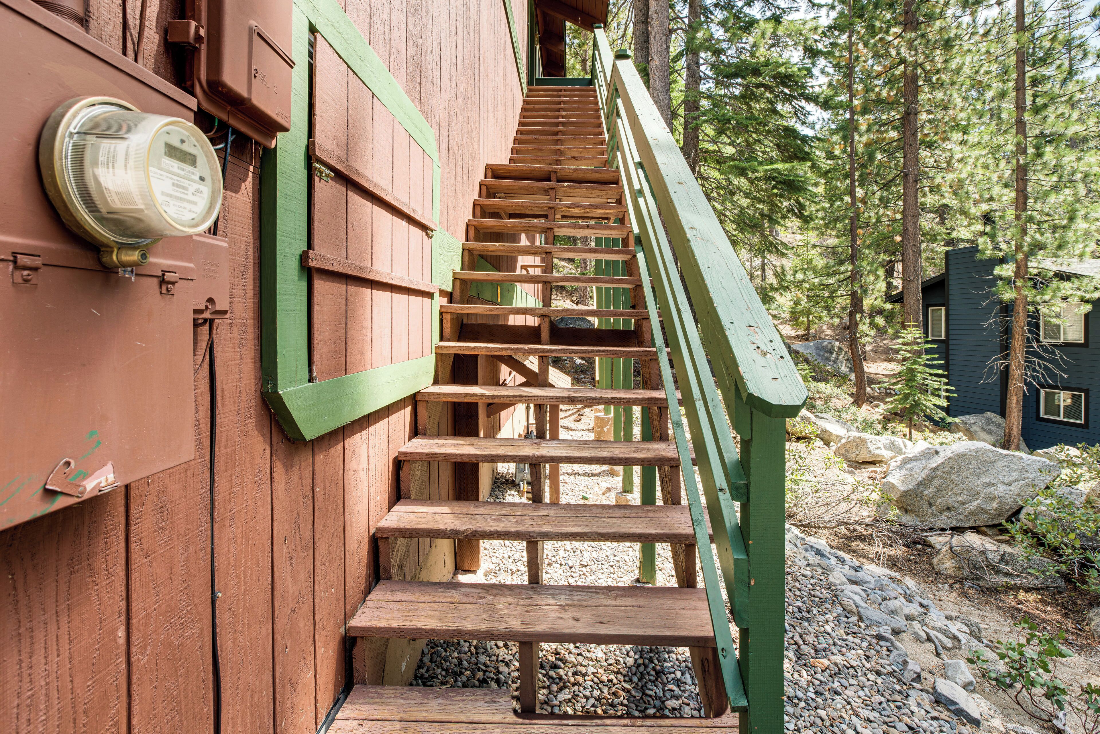 A wooden staircase with a green handrail leading to a building with a brown exterior.