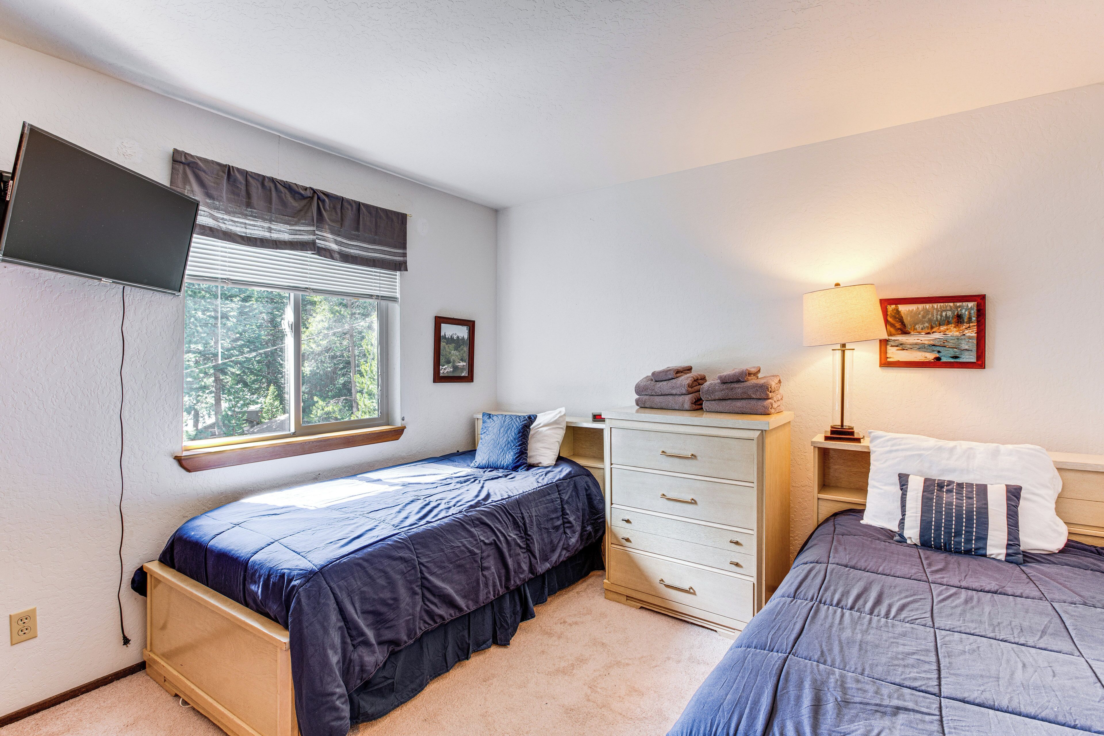 A bedroom with two beds, a dresser, a window with blinds, a lamp, and a painting on the wall.