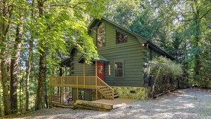 Eine rustikale Holzhütte mit einer Holzdiele und einer roten Tür, umgeben von dichtem Wald.