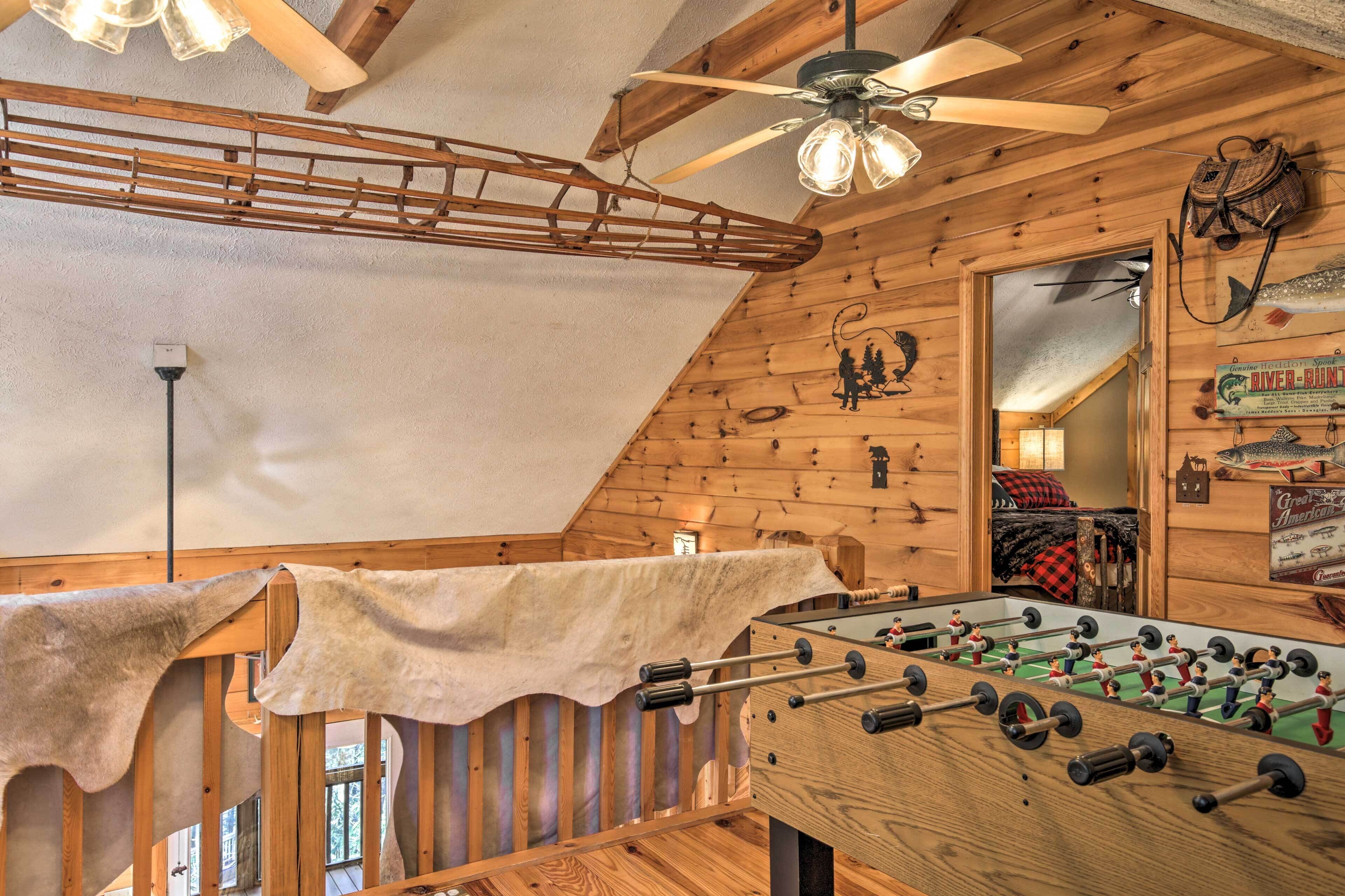 A wooden-floored room with a foosball table, a ceiling fan, and a loft area with a ladder.