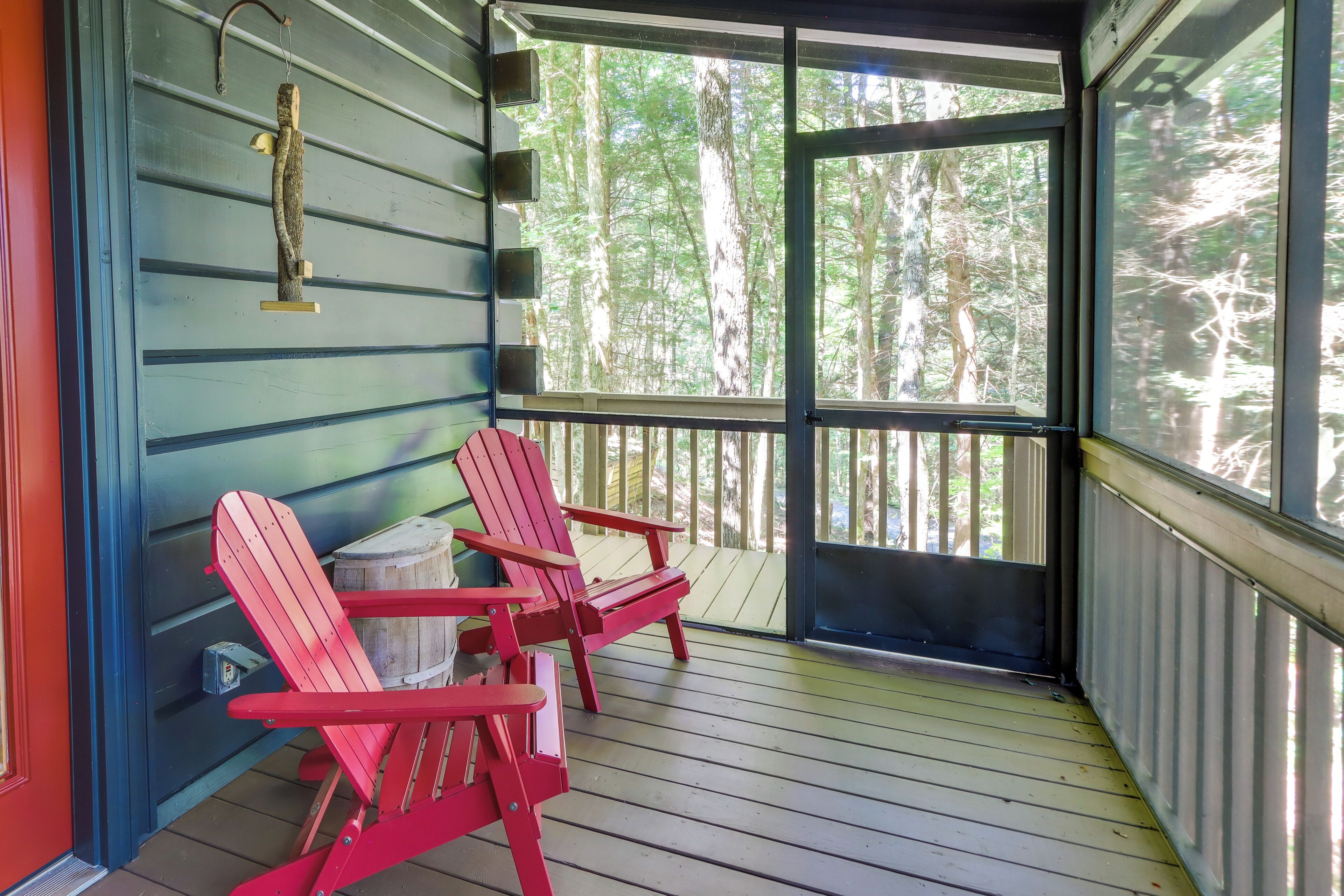 A porch with two red Adirondack chairs, a small table, and a hanging bird feeder.