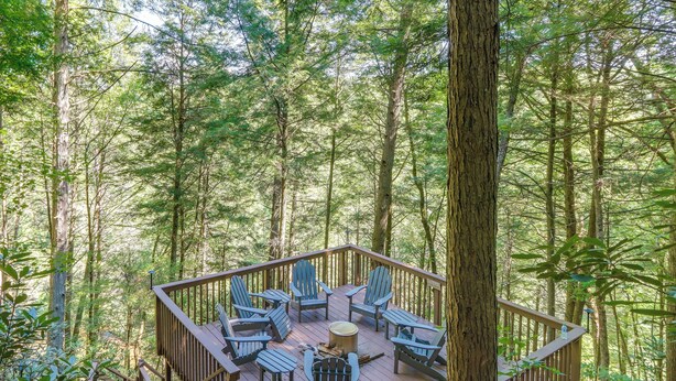 Eine Holzterrasse mit Adirondack-Stühlen und einer Feuerstelle, umgeben von einem Wald.
