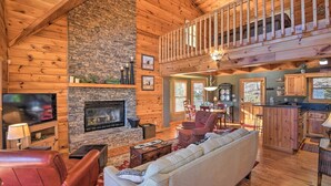 A cozy log cabin interior with a stone fireplace, wooden ceiling, and a dining area.