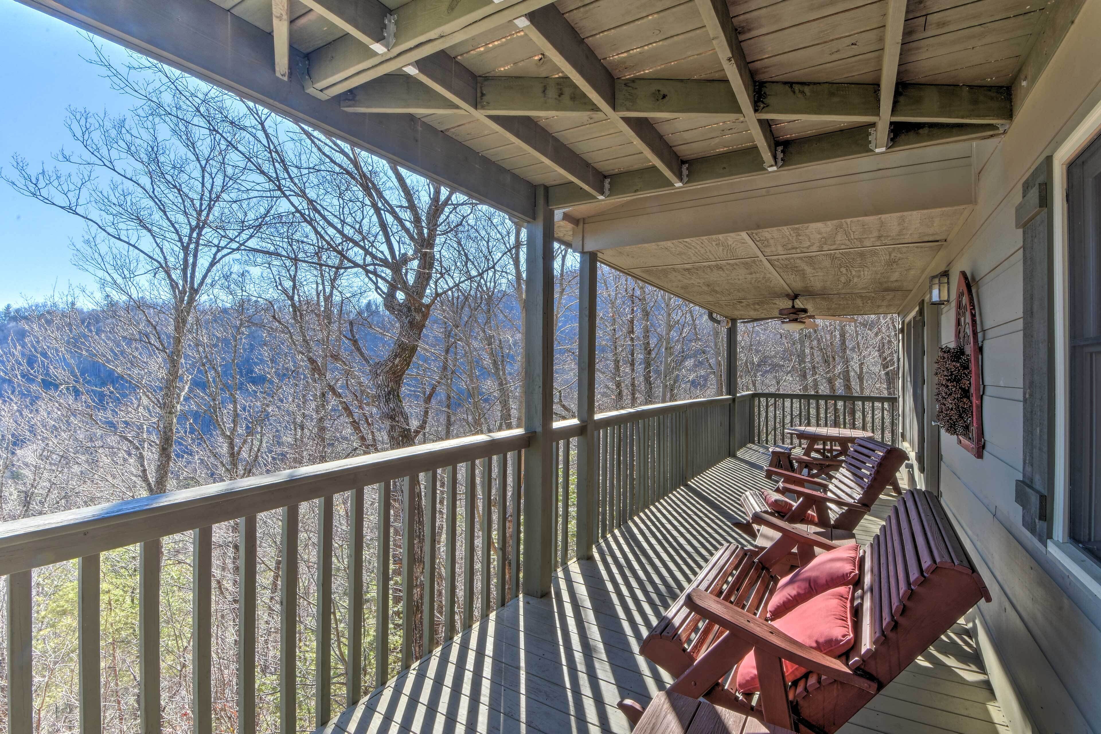 Een overdekt terras met houten banken en een balustrade, met uitzicht op een bergachtig landschap.