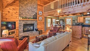 A spacious living area with a stone fireplace, wooden ceiling, and a balcony.