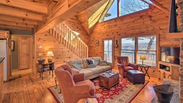 A cozy cabin interior with a wooden staircase, a sofa, a chair, a coffee table, and a fireplace.