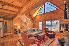 A cozy cabin interior with a wooden staircase, a sofa, a chair, a coffee table, and a fireplace. - Cozy Mountain Cabin - Panoramic Mountain Views (Blairsville)